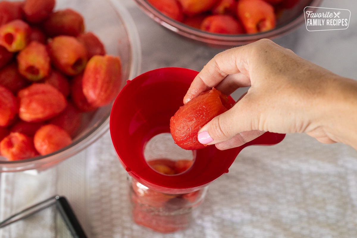 Placing a tomato into a jar with a canning funnel.