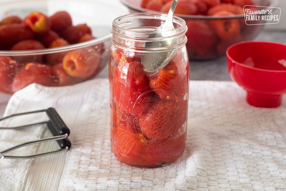 Pressing down whole tomatoes in a canning jar with a spoon.