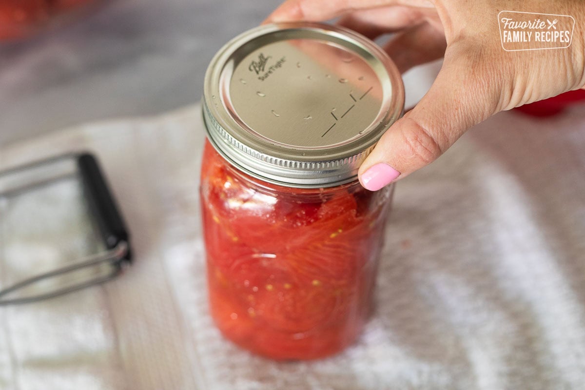 Tightening the rim of a canning jar of tomatoes.