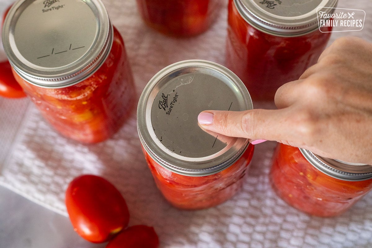 Finger pressing on top of canning jar of whole tomatoes.