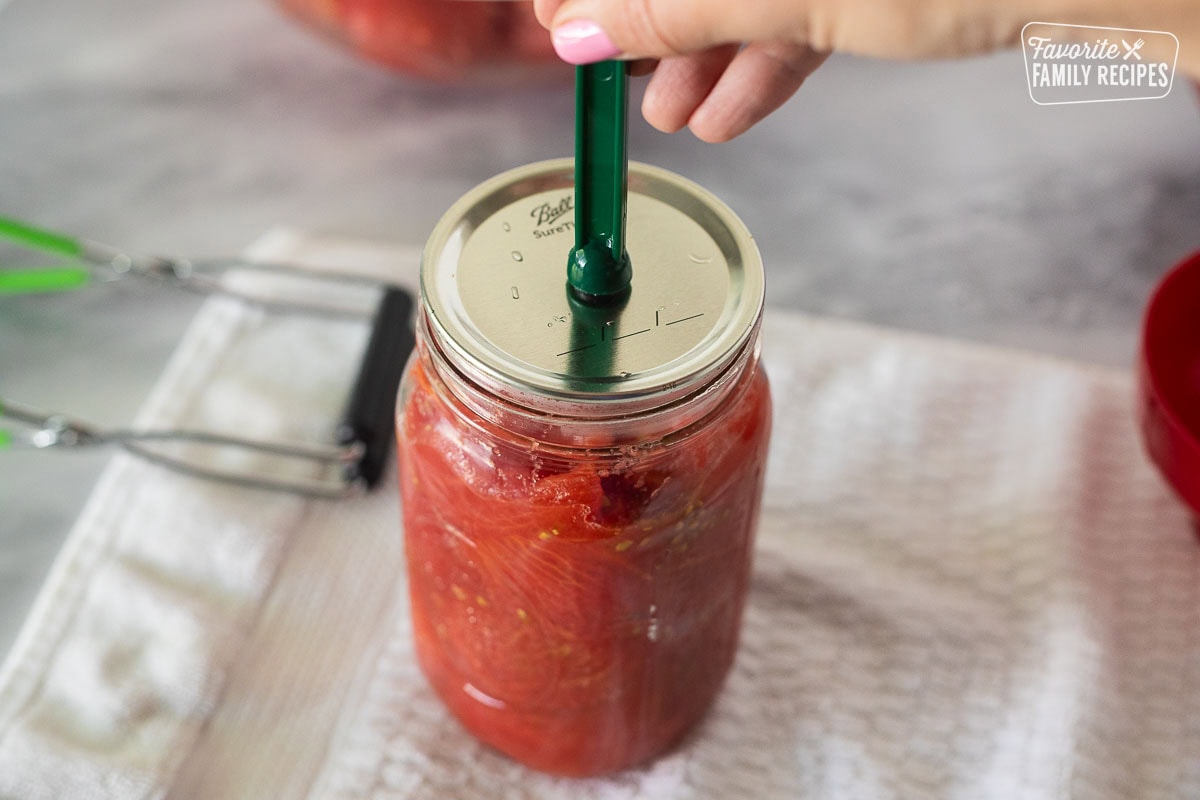 Placing lid on a jar of tomatoes with a lid lifter.