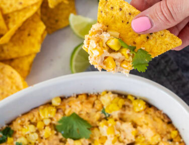 Hand holding a chip with Mexican Street Corn Dip in a dish.