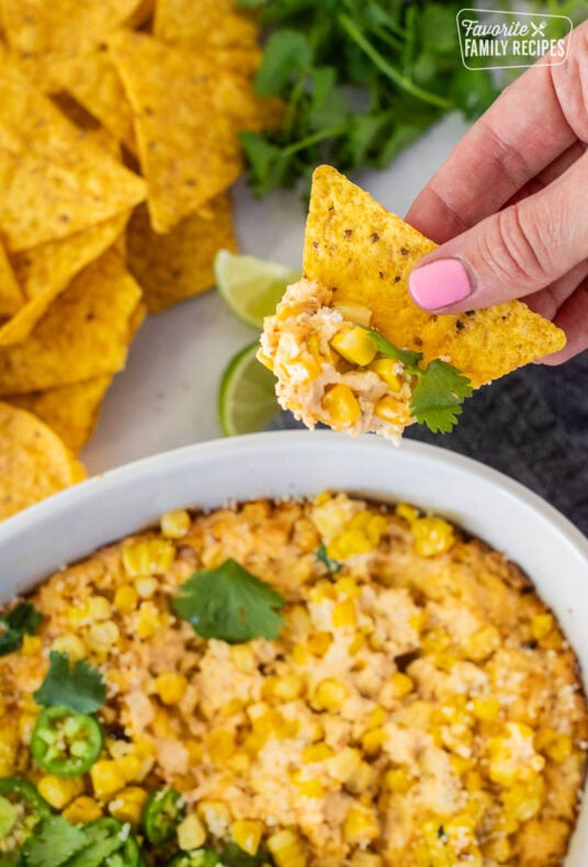 Hand holding a chip with Mexican Street Corn Dip in a dish.