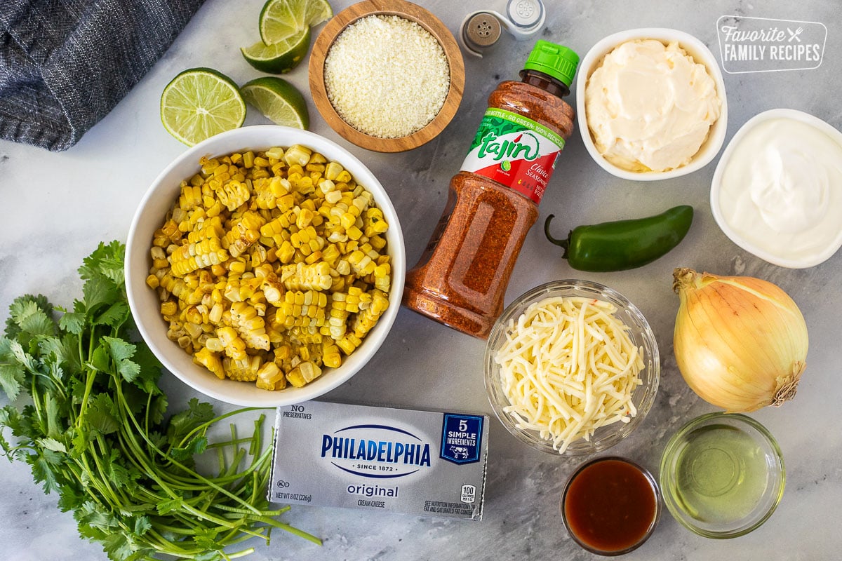 Ingredients to make Mexican Street Corn Dip including sour cream, mayonnaise, jalapeño, onion, oil, pepper jack cheese, Tajin seasoning, cojita cheese, cilantro, cream cheese, hot sauce, salt, pepper and lime.