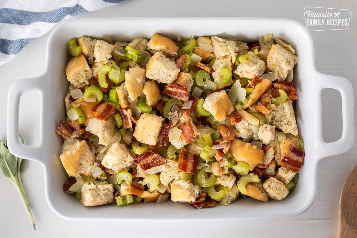 Baking dish with unbaked bacon stuffing. Wooden spoon on the side.