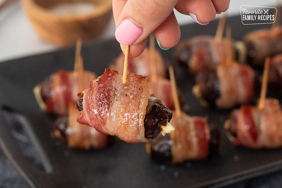 Hand holding a Bacon Wrapped Date Appetizer stabbed with a toothpick.