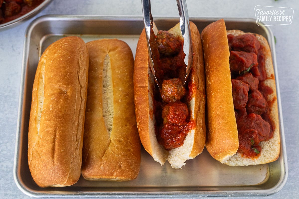 Placing meatballs into cut rolls with tongs.