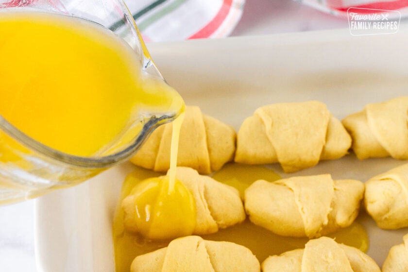 Pouring butter mixture over Apple Dumplings in a baking dish.