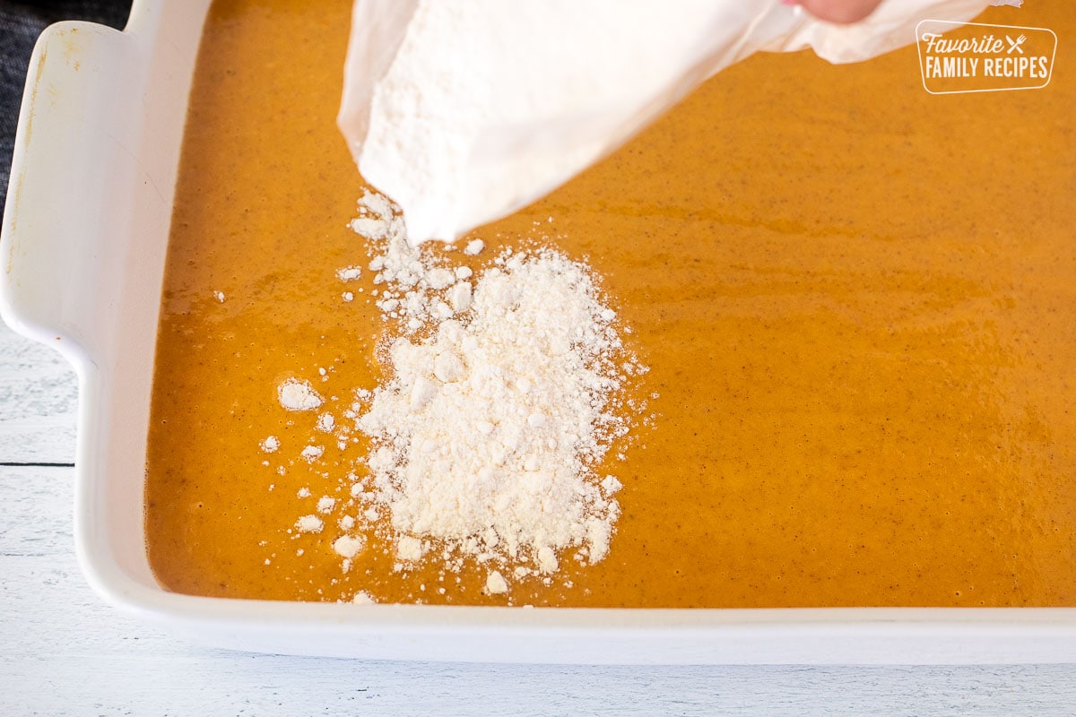 Placing cake mix over pumpkin mixture in a baking dish.