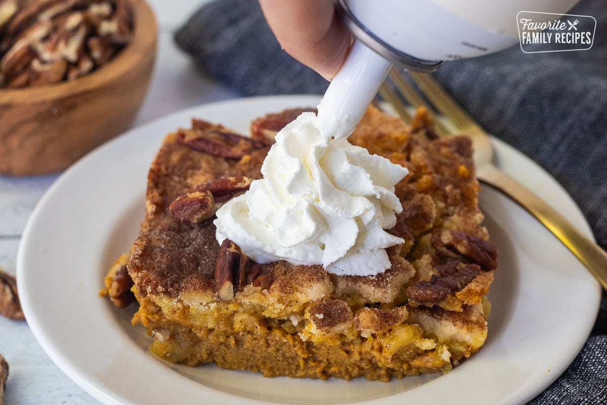 Squirting canned whipped cream over a slice of pumpkin cobbler on a plate.