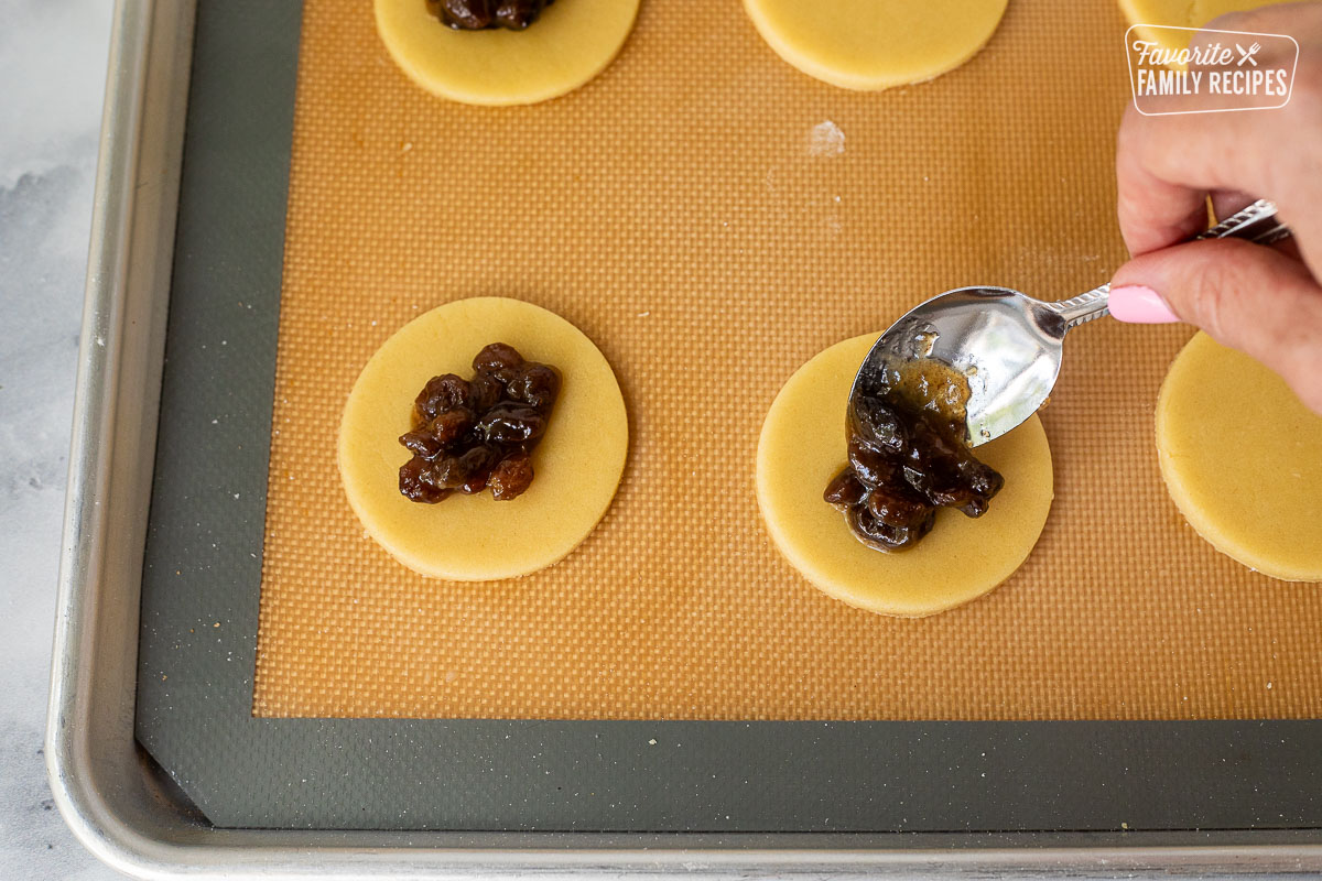 Spoon placing raisin mixture into round cookie dough.