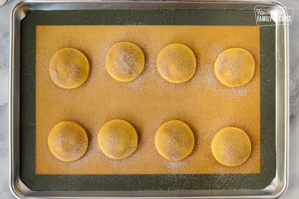 Sprinkled cinnamon sugar on top of unbaked cookies on a baking sheet.