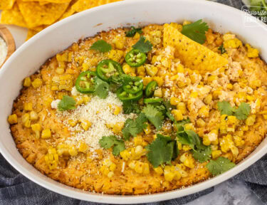 Baked Mexican Street Corn Dip in a dish toped with jalapeño, cilantro and cojita cheese with tortilla chips.