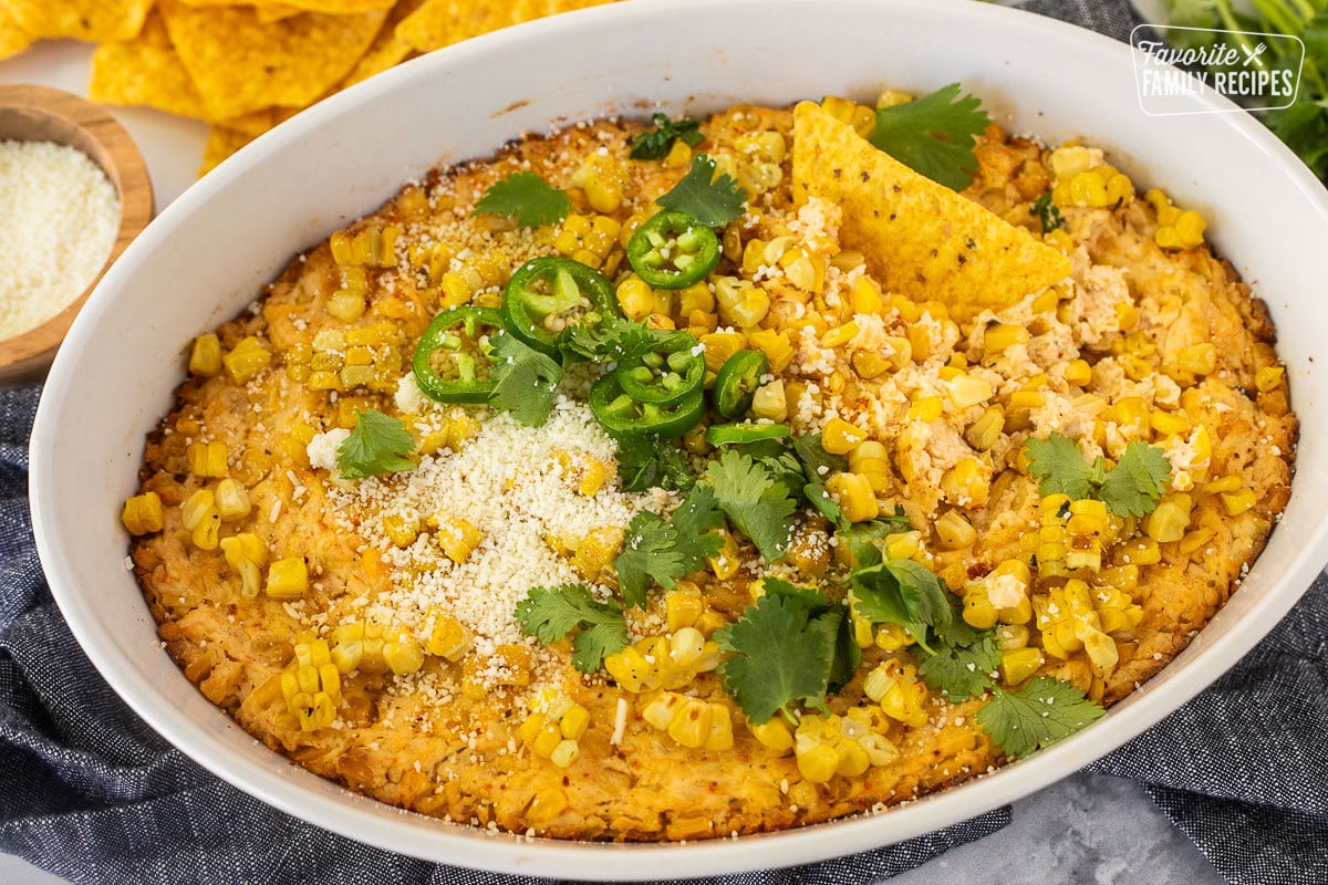 Baked Mexican Street Corn Dip in a dish toped with jalapeño, cilantro and cojita cheese with tortilla chips.