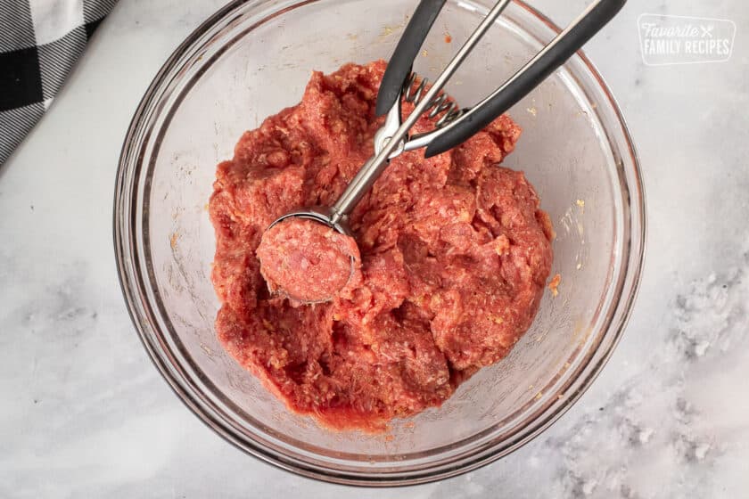 Ice cream scoop with meatball mixture in a bowl.