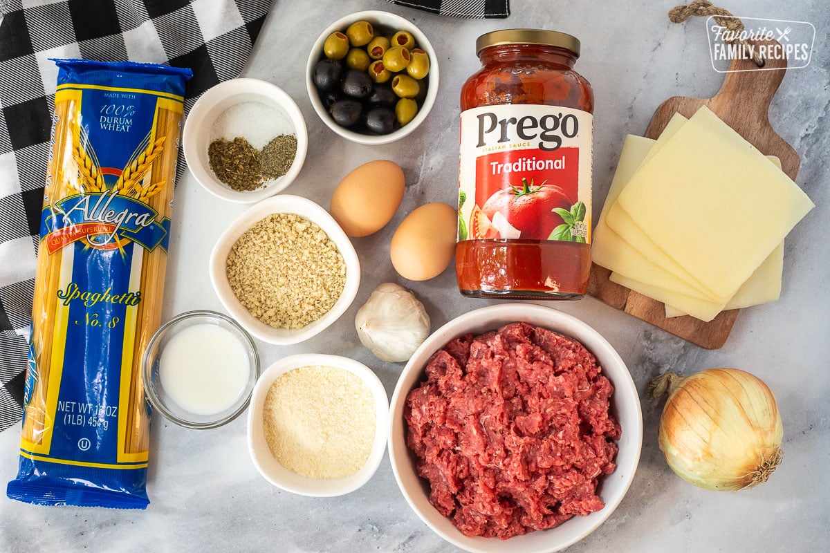 Ingredients to make Spaghetti and Eyeballs including ground beef, tomato sauce, mozzarella cheese, onion, eggs, garlic, parmesan cheese, panko bread crumbs, green olives, black olives, milk, spices and spaghetti pasta noodles.