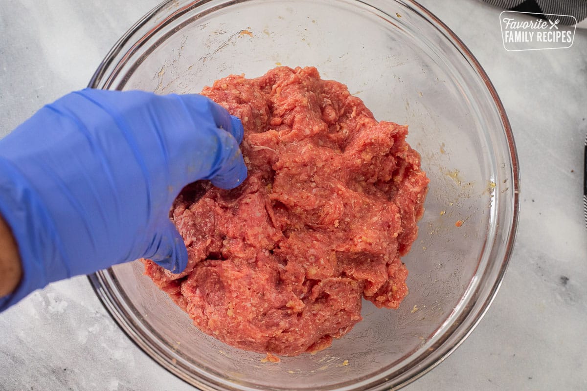 Hand mixing ground beef meatball mixture in a bowl.