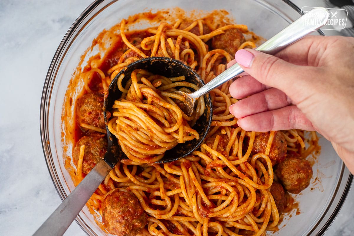 Hand twirling spaghetti noodles in ladle to make nests.