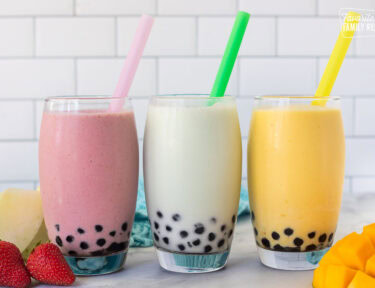 Strawberry, honeydew melon and mango boba smoothies in glasses with colorful large straws.