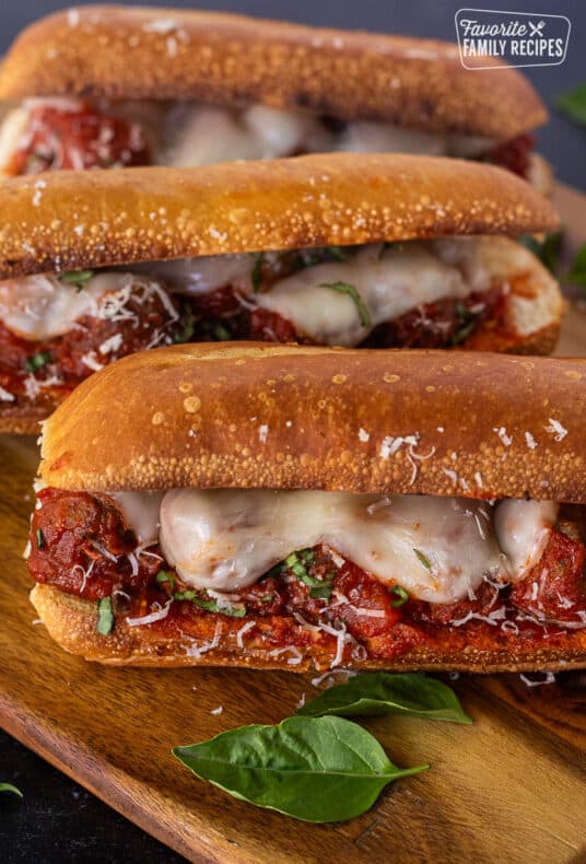 Three Meatball Sandwiches with melted cheese, fresh basil and grated parmesan on a toasted roll.