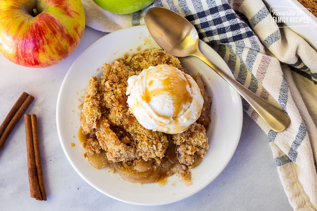 Apple Crisp resting on a plate with vanilla ice cream and caramel sauce. Spoon is also resting on the plate.