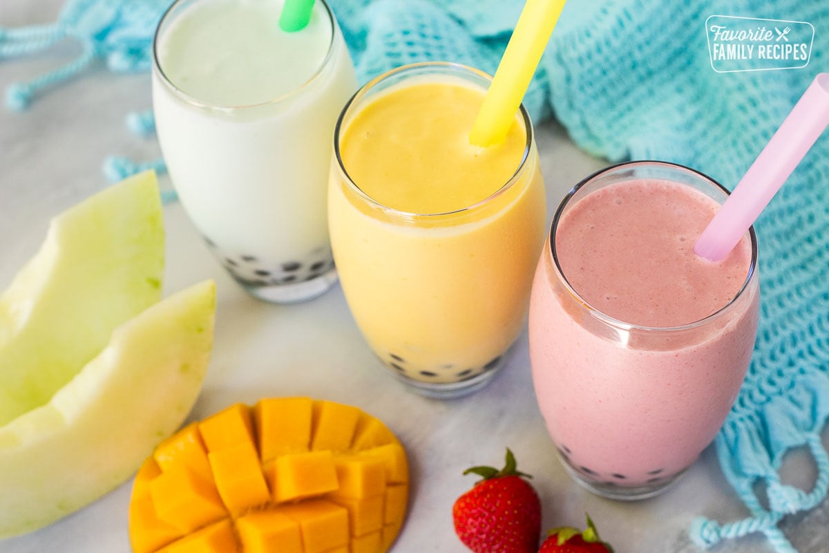 Strawberry, honeydew melon and mango boba smoothies in glasses with colorful large straws.