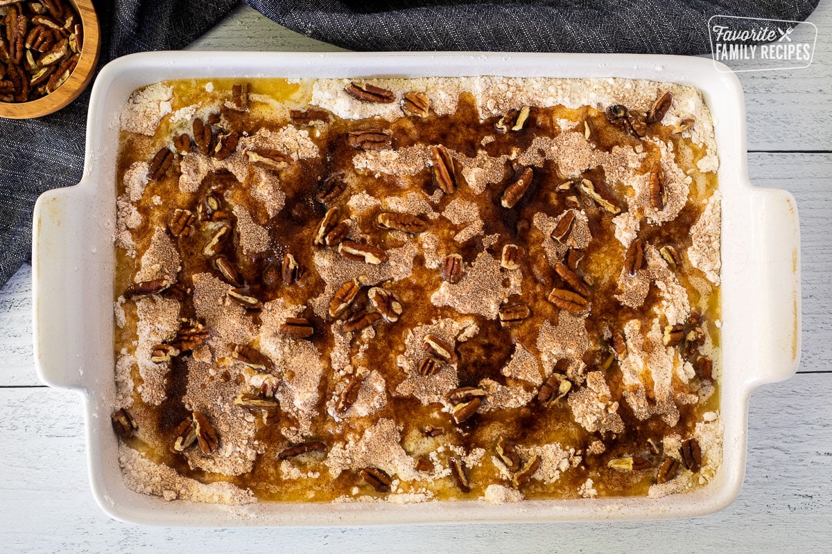 Baking dish with melted butter, pecans and cinnamon sugar on top of cake mixture and pumpkin mixture.