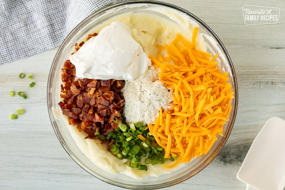 Mixing bowl with mashed potatoes, shredded cheddar cheese, sliced green onions, chopped bacon, sour cream and Ranch dressing seasoning.