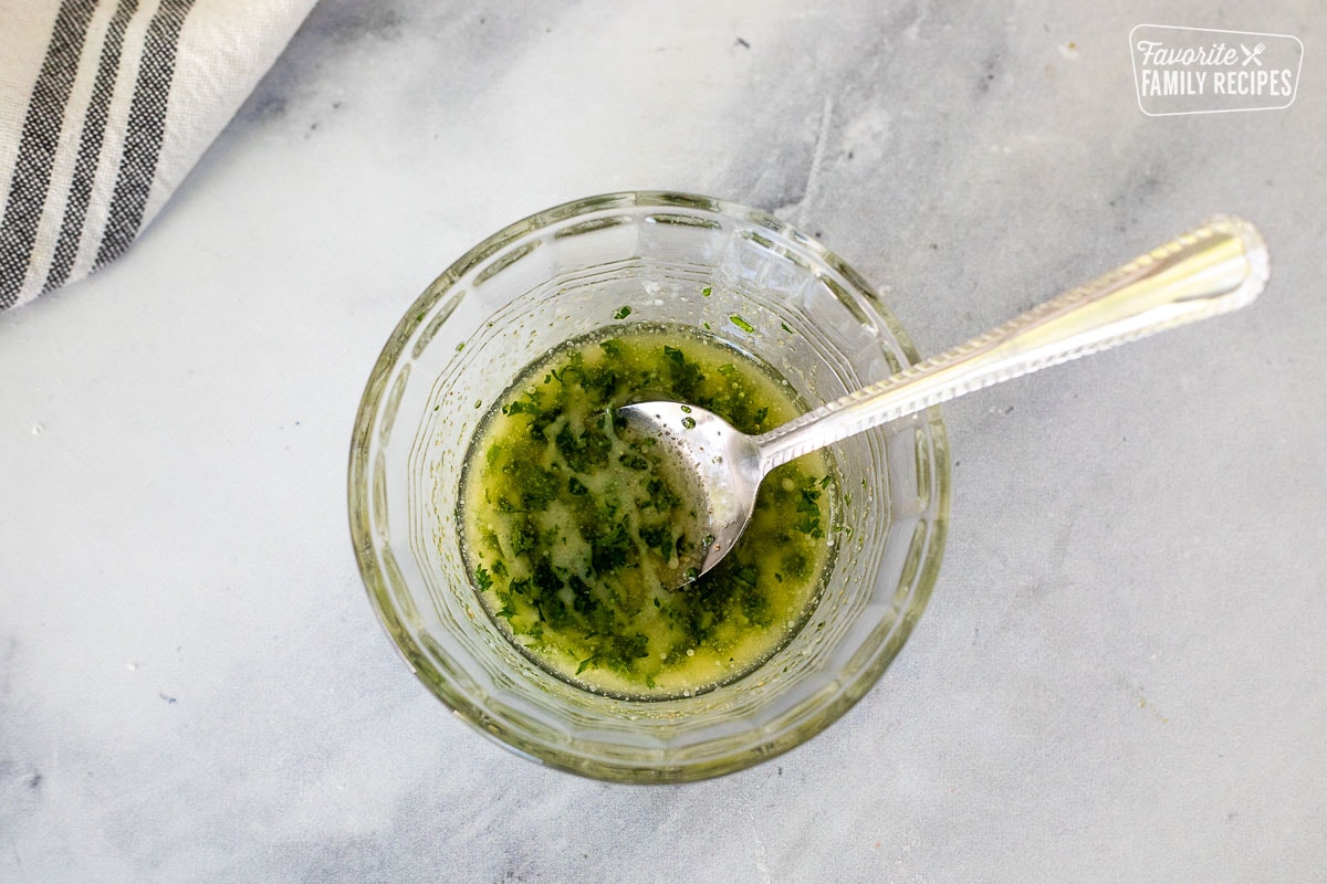 Glass mixing bowl with melted butter and parsley combined.