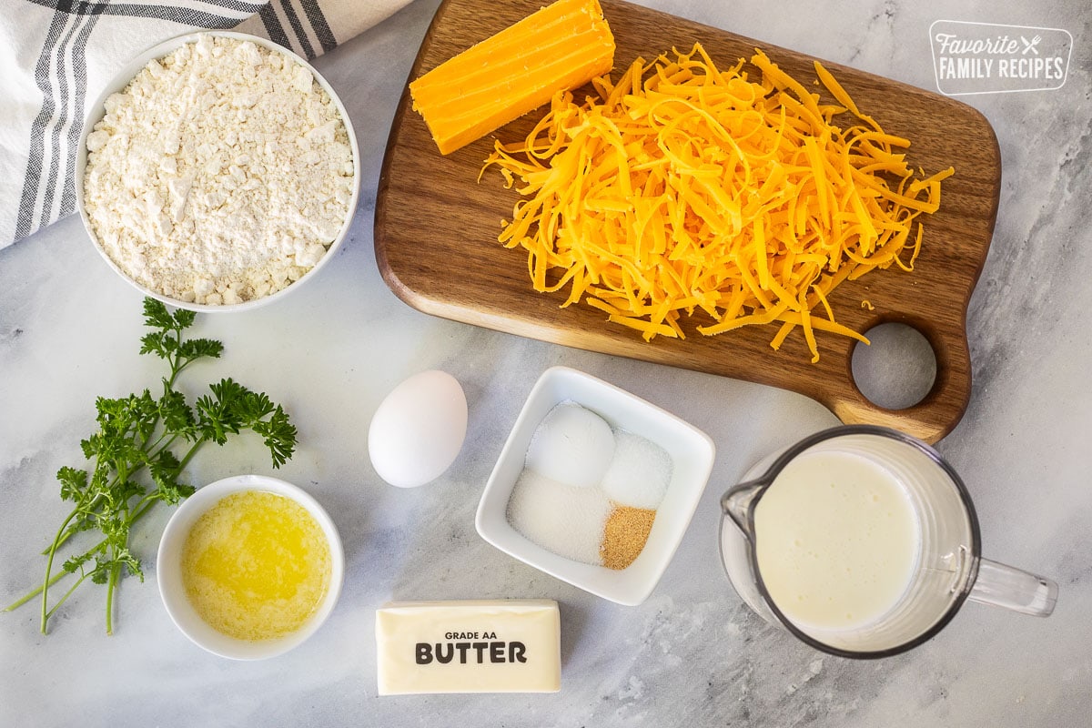 Ingredients to make Cheddar Bay Biscuits including shredded cheddar cheese, flour, egg, spices, buttermilk, frozen butter, melted butter and parsley.