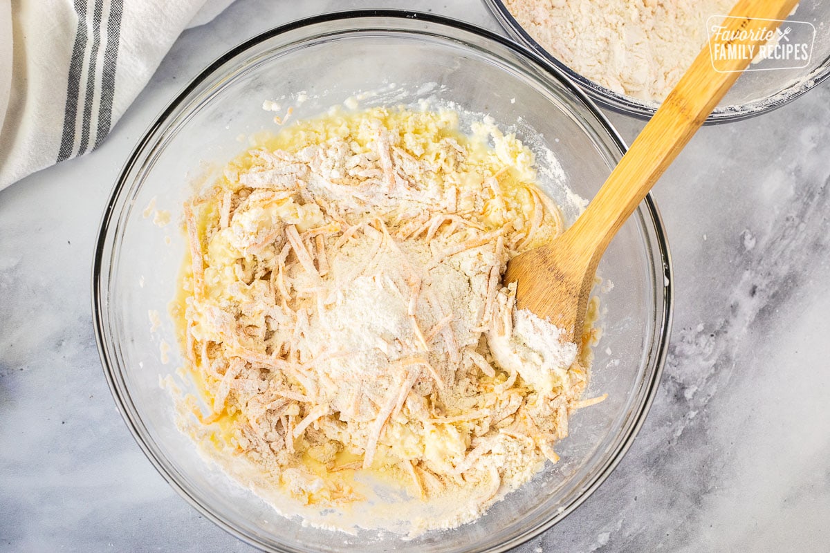 Mixing Cheddar Bay Biscuit ingredients together in a glass bowl with a wooden spoon.