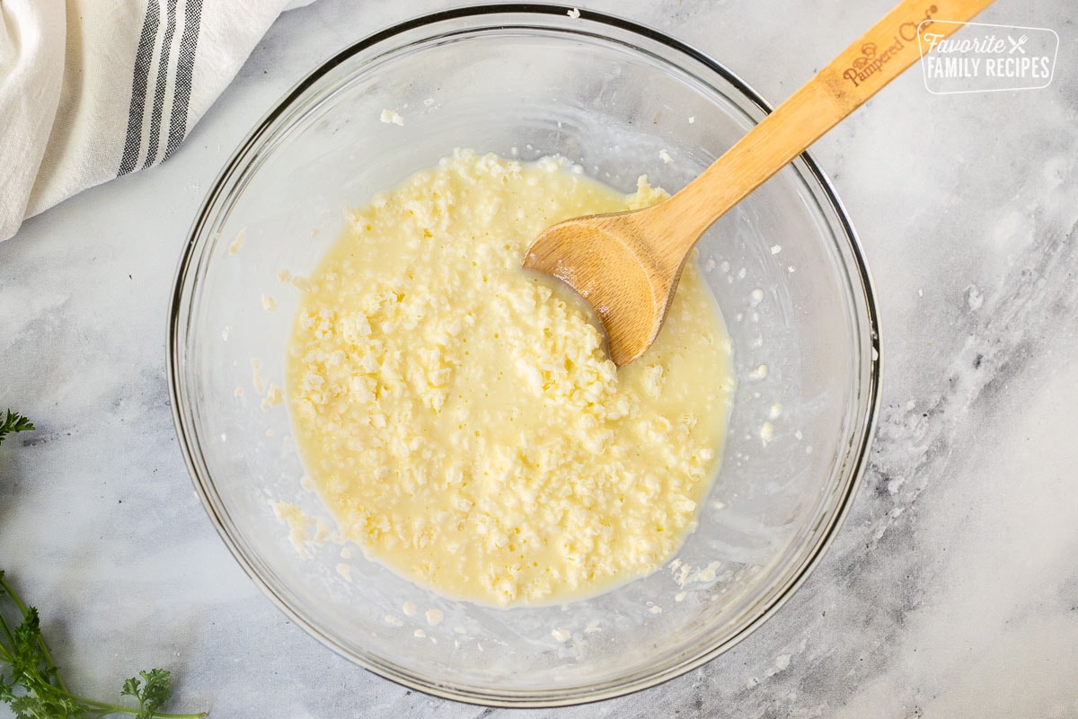 Glass bowl with wet ingredients combined with a wooden spoon.