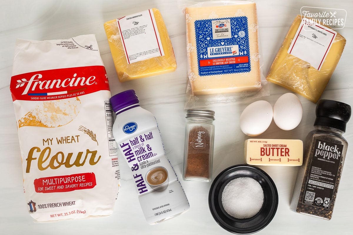 Ingredients to make Cheese Pie including half and half, flour, nutmeg, salt, black pepper, butter, egg, appenzeller cheese, gruyere cheese and Swiss immentaler cheese.