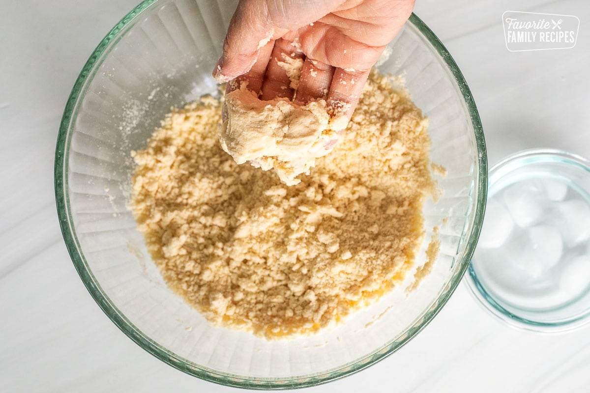 Hand holding pressed part of dough together over bowl.