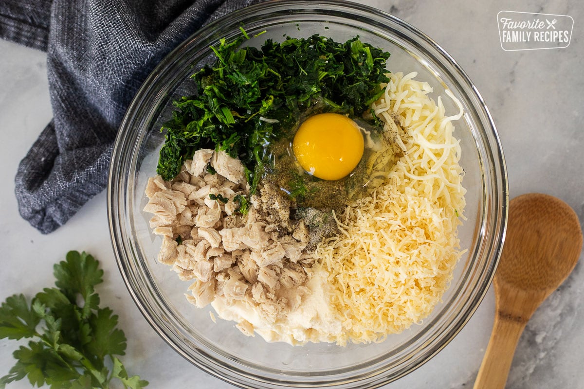 Glass bowl of ricotta cheese, mozzarella cheese. parmesan cheese. egg, spinach, chicken, salt and pepper.