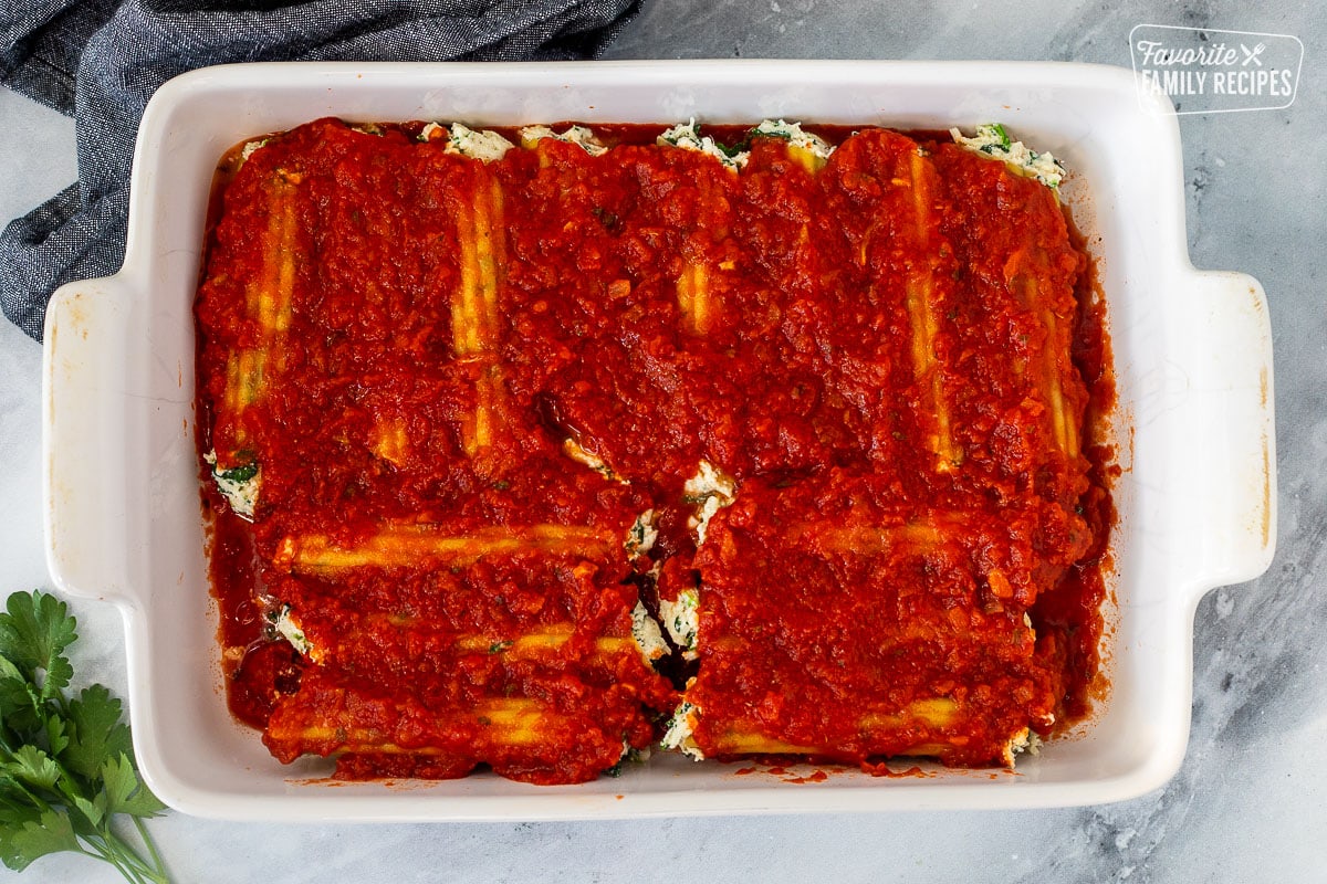 Baking dish with unbaked filled manicotti and topped with marinara sauce.