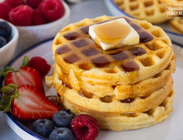 Easy homemade waffles stacked on a plate with butter and syrup. Fresh berries on the side.