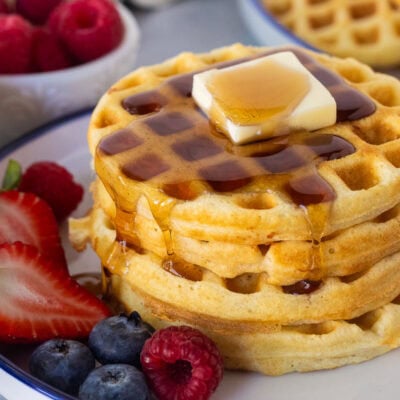 Easy homemade waffles stacked on a plate with butter and syrup. Fresh berries on the side.