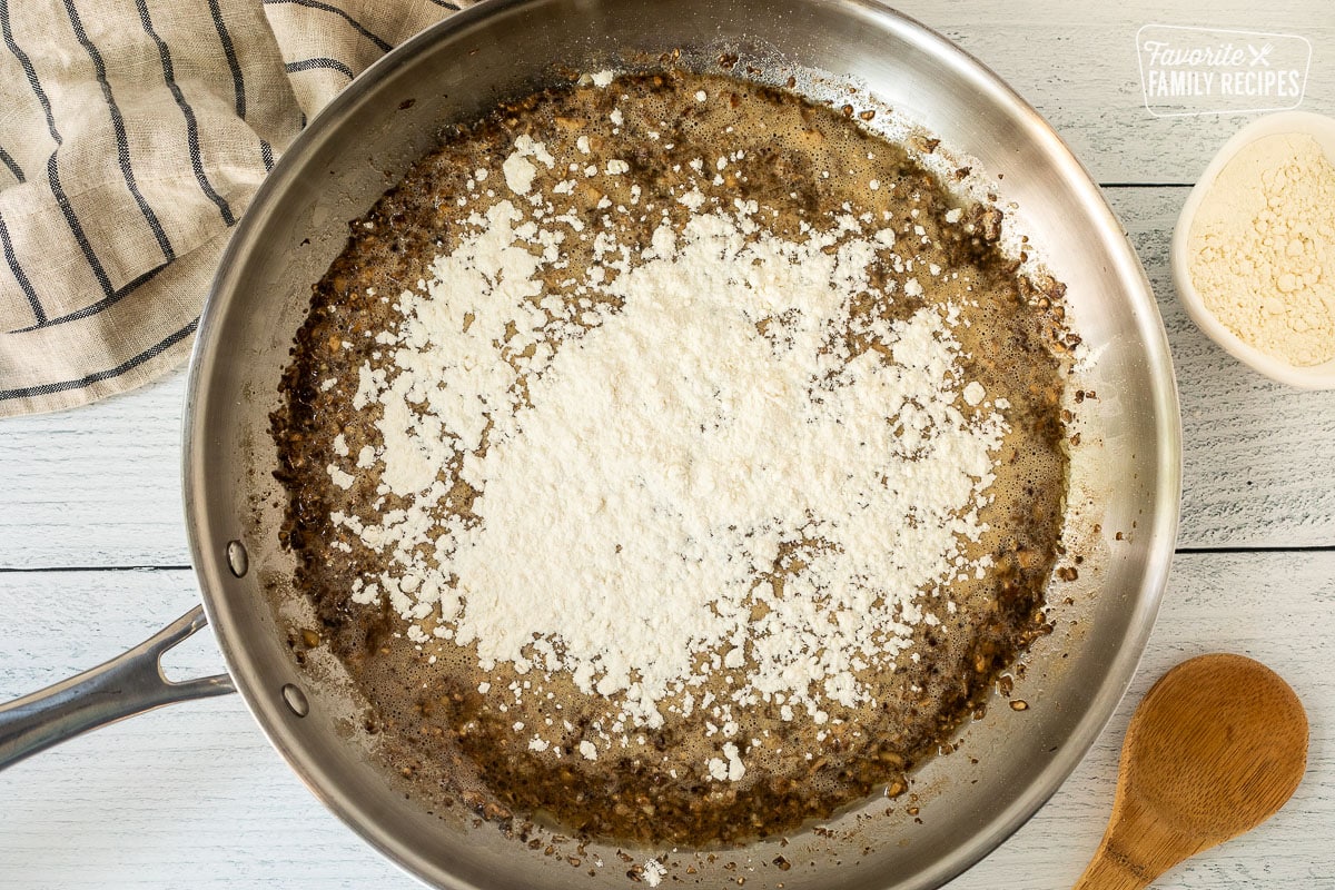 Flour on top of sautéed mushrooms in skillet.