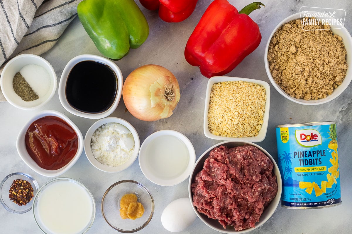 Ingredients to make crockpot, sweet and sour meatballs, including green, bell pepper, two red, bell peppers, brown sugar, crushed crackers, pineapple, tidbits, ground, beef, onion, egg, white vinegar, ginger, cornstarch, soy sauce, salt, pepper, milk and red pepper flakes.