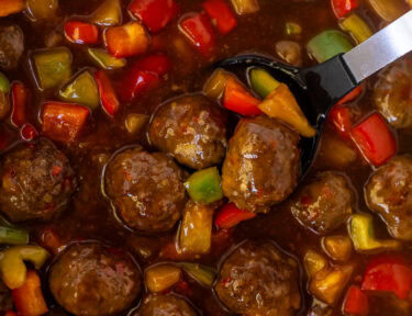 Spoon resting in a Crock pot of sweet and sour meatballs.