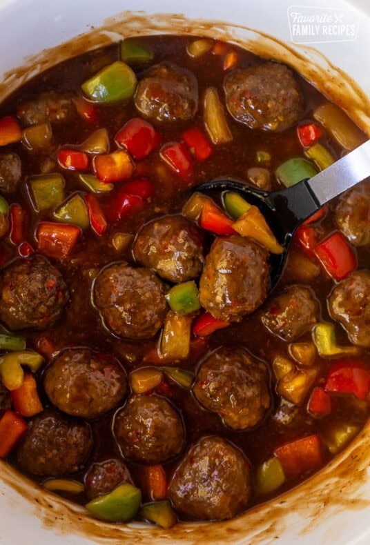 Spoon resting in a Crock pot of sweet and sour meatballs.