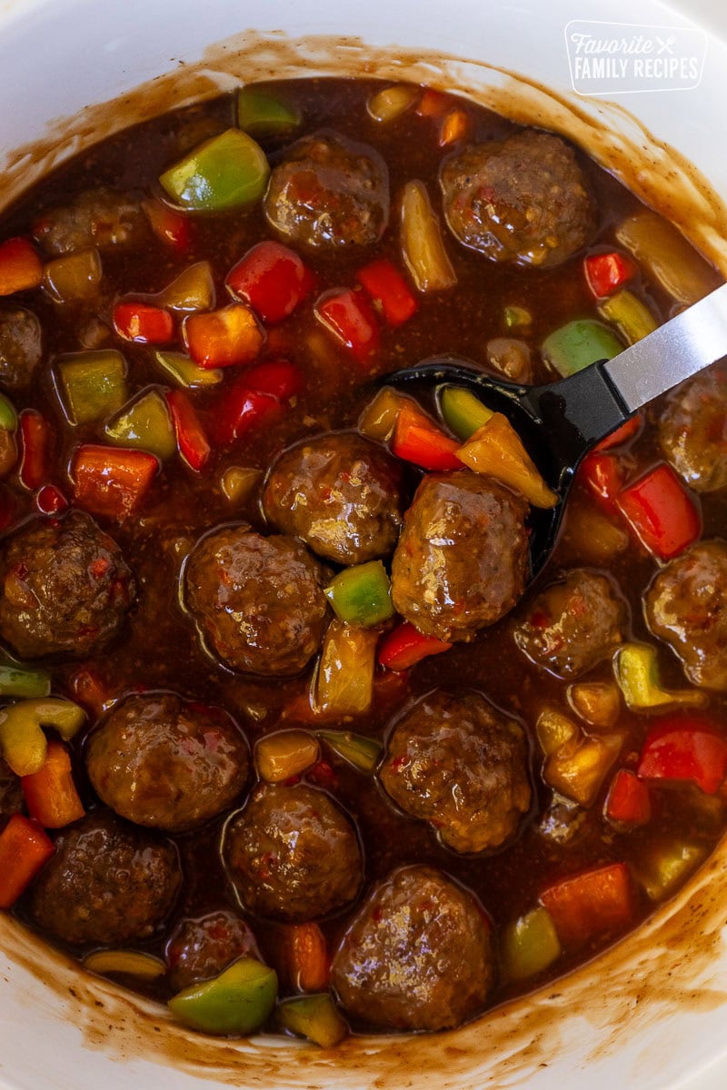 Spoon resting in a Crock pot of sweet and sour meatballs.