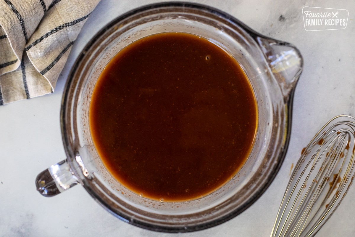 Glass mixing bowl with sweet and sour sauce and a whisk on the side.