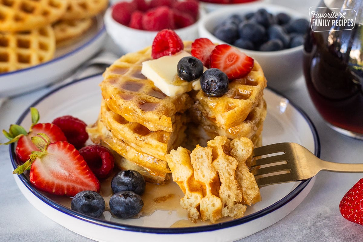 Cut stack of waffles with a fork. Fresh berries on the side.