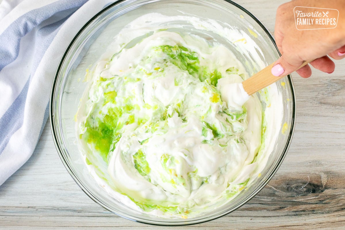 Mixing bowl with cool whip combined with pistachio pudding and pineapple mix.