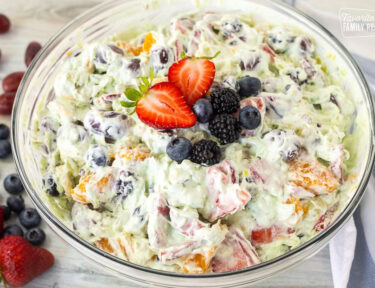 Glass mixing bowl with Easy Fruit Salad topped with strawberry, blackberries and blueberries.