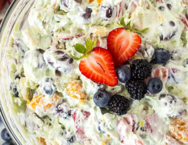 Glass mixing bowl with Easy Fruit Salad topped with strawberry, blackberries and blueberries.