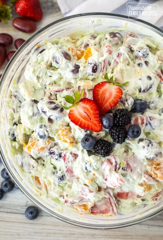 Glass mixing bowl with Easy Fruit Salad topped with strawberry, blackberries and blueberries.