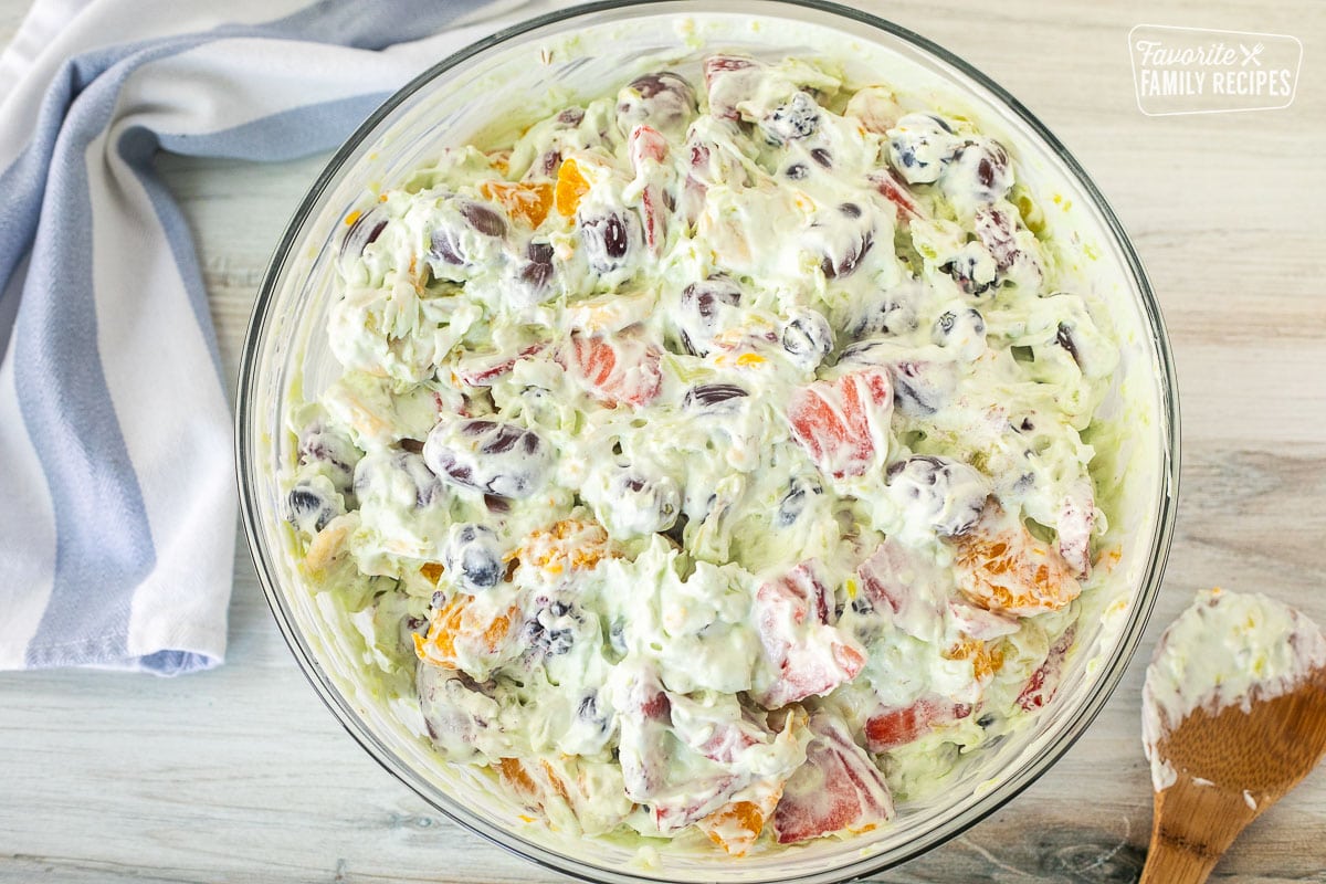 Glass mixing bowl with Easy Fruit Salad. Wooden spoon on the side.